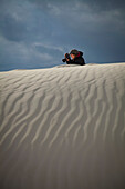 Female photographer takes a picture with white sand in the foreground, White Sands National Monument; Alamogordo, New Mexico, United States of America