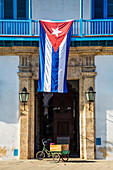 The national flag of Cuba hangs over the entrance to the Palace of the Artisans (Palacio de la Artesania), Old Town; Havana, Cuba