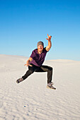 Carefree man in mid-air on the white sand with blue sky, White Sands National Monument; Alamogordo, New Mexico, United States of America