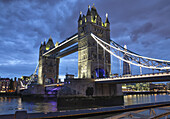 Tower Bridge in der Abenddämmerung beleuchtet und im ruhigen Wasser der Themse reflektiert; London, England.