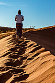 Weibliche Touristin geht eine Sanddüne hinauf, Elim-Düne, Namib-Wüste; Sesriem, Namibia.