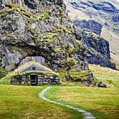 Barn built into a rocky mountainside, now overgrown with grass; Rangarping eystra, Southern Region, Iceland
