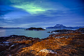 Die Nacht bricht über die zerklüftete Küste Grönlands herein, der Himmel leuchtet grün und spiegelt sich im ruhigen Wasser; Nuuk, Sermersooq, Grönland