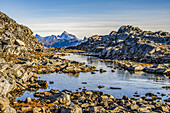 Rocky landscape with water and rugged mountain peaks in the distance; Sermersooq, Greenland