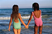 Back View of Two Girls in Swimwear, Holding Hands on Beach South Andros, The Bahamas