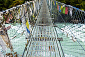 Gebetsfahnen auf beiden Seiten der Hängebrücke über den Dudh Koshi-Fluss entlang des Everest-Basislagers und des Gokyo-Treks; Solokhumbu-Distrikt, Nepal.
