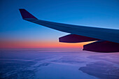 Detail eines Flugzeugflügels beim Überfliegen der arktischen Meere auf dem Weg nach Island mit einem leuchtend rosa Himmel am Horizont; Island