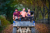 Three young adults sit in the back of a dune buggy with dogs after a muddy tour; Retaruke, Manawatu-Wanganui, New Zealand
