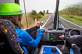 A girl sits in the front seat of a bus as they travel through New Zealand, Tongariro National Park; Manawatu-Wanganui, New Zealand