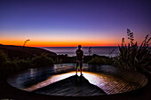 Ein Mann beobachtet den Sonnenuntergang von den Klippen von Raglan, Neuseeland; Raglan, Waikato, Neuseeland