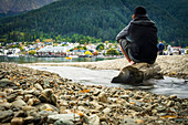 Ein Mann sitzt am Ufer des Lake Wakatipu in Queenstown und denkt nach; Queenstown, Otago, Neuseeland.
