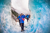 Reisende erkunden den berühmten Franz-Josef-Gletscher mit seinen blauen Eishöhlen, tiefen Gletscherspalten und Tunneln, die die sich ständig verändernden Eisformationen markieren; Westküste, Neuseeland