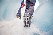 Close-up of person's feet wearing spiked traction cleats while walking on ice through the famous Franz Josef Glacier; West Coast, New Zealand