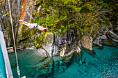 The Blue Pools of Makarora offer enticing blue waters to swim in. A man jumps off a bridge into the water in Mount Aspiring National Park; Makarora, New Zealand