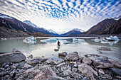 Man cautiously walking out into the water of the icy glacial lakes of Mount Cook National Park; Canterbury, New Zealand