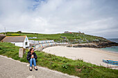 A young woman sits with a coffee mug looking out at the beach and coast of St. Ives, a small fishing village on the South Western tip of Cornwall, England. Colourful beach hotels sits on the shoreline; Saint Ives, Cornwall, England