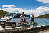 A group of friends standing and eating in the sun outside their camper van as they make a stop in Slano for an afternoon at the beach; Slano, Dubrovacko-neretvanska zupanija, Croatia