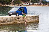 Women stop for an early morning swim and shower after camping in their van; Podgora, Split-Dalmatia County, Croatia