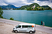 Reisende halten ihr Wohnmobil an, um ein Foto von der Kirche auf einer Insel (The Church of the Assumption) im Bleder See zu machen; Bled, Slowenien