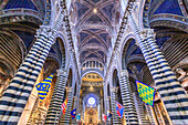 Bezirksfahnen von Siena schmücken die schwarz-weiß gestreiften Marmorsäulen und -bögen im Inneren des kunstvollen Doms von Siena; Siena, Provinz Siena, Toskana, Italien.
