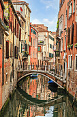 Small foot bridge spanning a side canal in-between colorful stone buildings; Venice, Venezia, Italy