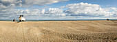 Paar steht am Ufer und schaut auf den Ozean neben einem hölzernen Kajütboot, das am Kiesstrand von Dungeness an der Atlantikküste festgemacht ist; Dungeness, Kent, England, Vereinigtes Königreich.