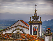Alter Glockenturm und Lehmziegeldächer mit Blick auf die Landschaft und die mittelalterliche Stadt Obidos bei dunstigem, bedecktem Himmel; Obidos, Estremadura, Region Oeste, Portugal.