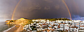 Regenbogen über dem traditionellen Fischerdorf Burgau unter einem stürmischen Himmel in der Gemeinde Vila do Bispo in der westlichen Region der Algarve; Burgau, Algarve, Portugal