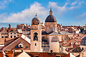 Overview of the tiled rooftops and the domes of the Clock Tower and the Dubrovnik Cathedral (Cathedral of the Assumption of the Virgin Mary) in the Old Town with a blue sky and the Adriatic Sea in the background; Dubrovnik, Dalmatia, Croatia