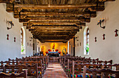 Innenansicht einer Kapelle mit Altar und Reihen von Holzstühlen in der historischen Mission Espada; San Antonio, Texas, Vereinigte Staaten von Amerika.