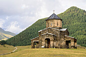 Alte Kirche der Heiligen Dreifaltigkeit in Schenako mit den bewaldeten Bergen des Großen Kaukasus im Hintergrund im Nationalpark Tuschetien; Schenako, Kachetien, Georgien.