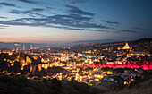 Die Dämmerung bricht über die Hauptstadt Tiflis herein. Die Lichter der Stadt heben die Dreifaltigkeitskathedrale von Tiflis auf der rechten Seite, die Brücke des Friedens über die Kura (Mtkvari-Fluss) in der Mitte und die alte Narikala-Festung auf der linken Seite der Skyline hervor; Tiflis, Georgien