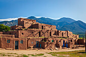 Atemberaubender Blick auf das rote Adobe Pueblo, Hlaauma (North House), ein alter Wohnkomplex im Taos Pueblo, der noch immer vom indigenen Volk der Tiwa bewohnt wird und in dem im Laufe der Jahre bunte Türen und Fenster eingebaut wurden, vor der Kulisse der Taos Mountains (Sangre de Cristo Range). Es gilt als eine der ältesten durchgehend bewohnten Gemeinden in den Vereinigten Staaten; Taos, New Mexico, Vereinigte Staaten von Amerika
