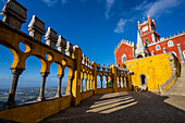 Overlooking Sintra through the colorful arches and columns of Queen's Terrace with the red Clock Tower in the background at Palacio Da Pena; Sintra, Lisbon District, Portugal
