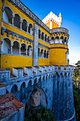 Bemalte, überdachte Balkone und Turm am Palacio Da Pena mit den zinnenbewehrten Steinmauern darunter; Sintra, Bezirk Lissabon, Portugal