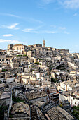 Cityscape of the mountaintop town of Sassi di Matera and its ancient cave dwellings with the bell tower of the Matera Cathedral overlooking the city; Matera, Basilicata, Italy