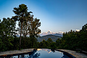 Machhapuchhare Peak, the Fish Tail Mountain reflected in an infinity pool at a mountain lodge from the Pokhara Valley of the Himalayas; Pokhara, Pokhara Valley, Nepal