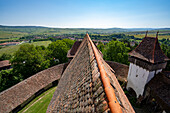 Close-up of the tiled rooftop of the Viscri Fortified Saxon Church with its surrounding stone wall and an overview of the village and countryside; Viscri, Brasov County, Transylvania, Romania