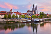 Outlook over the Danube River with steamboats docked along the riverfront and the Gothic St Peter's Cathedral from the Marc?-Aurel-shore in the Old Town of Regensburg at sunset with a pastel hues; Regensburg, Bavaria, Germany