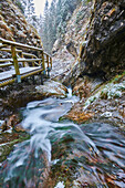 Close-up of snowy flowing river with a footbridge curving around the rocky canyon at Janosikove Diery in winter; Little Fatra (Kleine Fatra), Carpathian Mountains, Terchova, Slovakia
