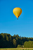 Gelber Heißluftballon in klarem, blauem Himmel, der von einem Feld abhebt; Bayern, Deutschland