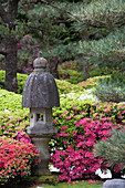 A Stone Lantern With Flowers And Trees In The Background; Portland Oregon United States Of America