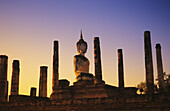 Thailand, Sukhothai, Wat Mahathat, Buddha Statue With Many Pillars At Sunset, Blue And Orange Sky.