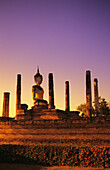 Thailand, Sukhothai, Glowing sunlight on structure of Buddha statue with many pillars at sunset; Wat Mahathat