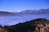 Nepal, Distant view of niva lodge on Hillside with cloud line and central Himalayas in background; Nagarkot