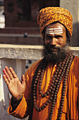 Nepal, Kathmandu Valley, Hinduistischer heiliger Mann in orangefarbenem Gewand und Turban, lächelnd und mit der Hand gestikulierend. Nur für redaktionelle Zwecke.