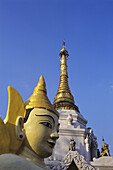 Burma (Myanmar), Yangon, Nahaufnahme der Buddha-Statue und der Spitze des Tempels vor blauem Himmel; Schewedagon Paya