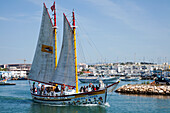 A Boat With Large Sails Travels Through The Harbour; Lagos Algarve Portugal