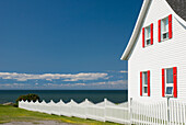 Weißes Haus mit roter Umrandung und weißem Lattenzaun am Meer; Gaspesie Quebec Kanada