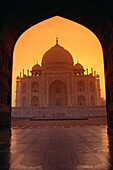 Indien, Agra, Blick auf das Taj Mahal durch den Torbogen eines benachbarten Gebäudes, oranger Sonnenuntergang